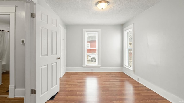 unfurnished room featuring a textured ceiling, baseboards, and wood finished floors