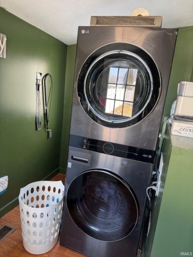 laundry room featuring stacked washer and dryer, laundry area, wood finished floors, visible vents, and baseboards