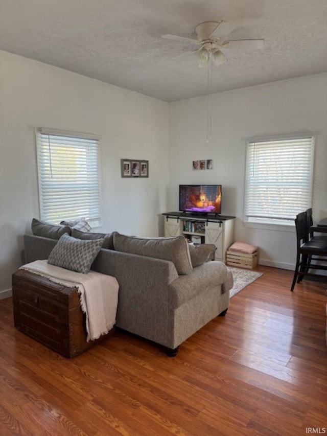 living area with ceiling fan, a textured ceiling, baseboards, and wood finished floors