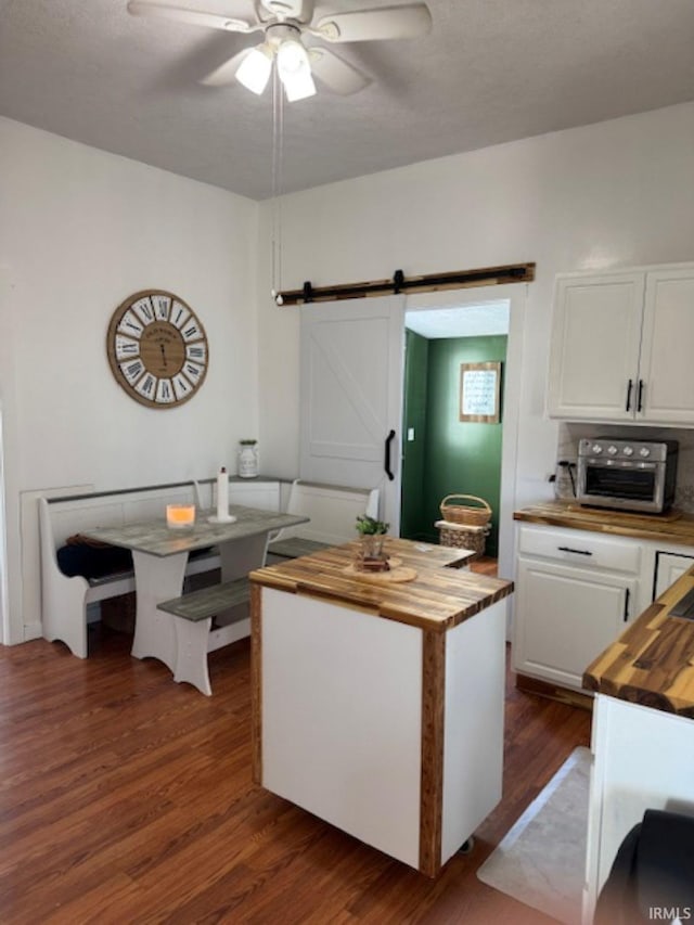 kitchen with a barn door, butcher block counters, a ceiling fan, white cabinets, and dark wood-style floors