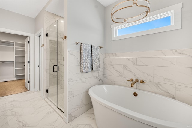 full bath featuring a freestanding tub, tile walls, marble finish floor, a spacious closet, and a shower stall