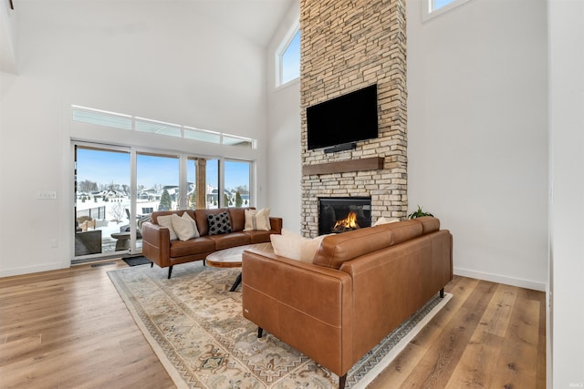 living room with light wood finished floors, a stone fireplace, and baseboards