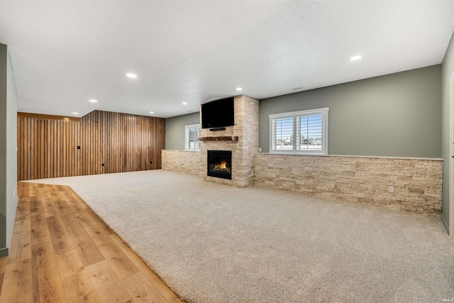 unfurnished living room featuring a textured ceiling, recessed lighting, light carpet, a fireplace, and wainscoting