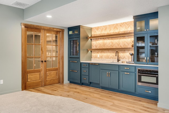 bar featuring light wood finished floors, visible vents, wet bar, a textured ceiling, and a sink