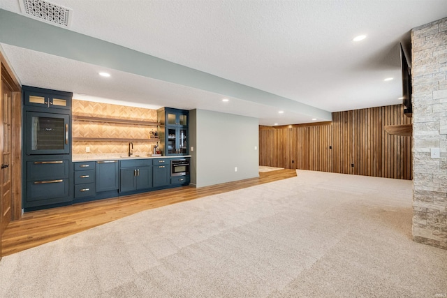 bar with indoor wet bar, visible vents, stainless steel oven, wooden walls, and a textured ceiling