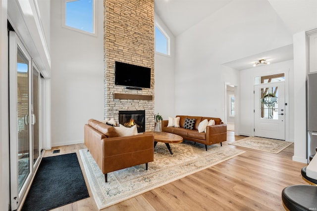 living area with high vaulted ceiling, a stone fireplace, light wood-style flooring, and baseboards