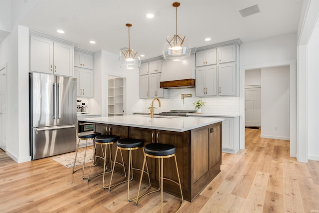 kitchen with a center island with sink, light countertops, freestanding refrigerator, a sink, and a kitchen breakfast bar