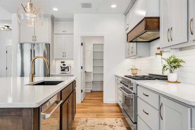 kitchen with a sink, light wood-type flooring, backsplash, high end appliances, and pendant lighting