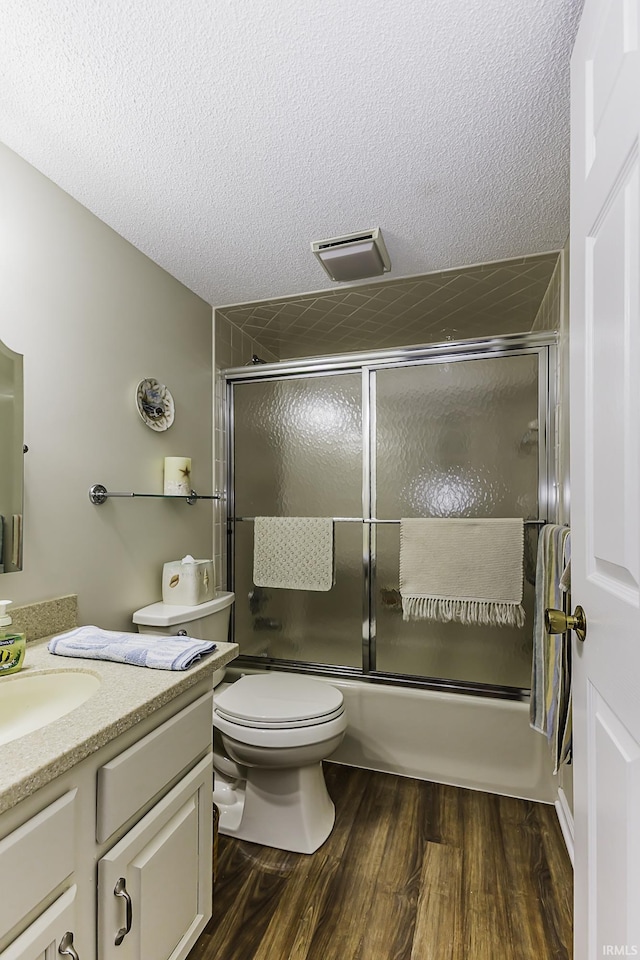 full bathroom featuring a textured ceiling, toilet, wood finished floors, vanity, and combined bath / shower with glass door