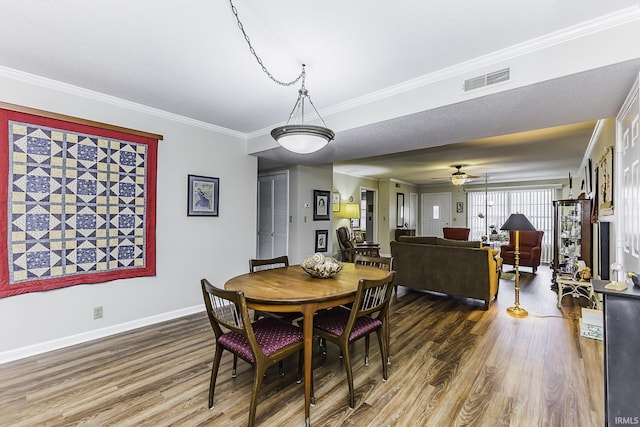 dining area with baseboards, wood finished floors, visible vents, and crown molding