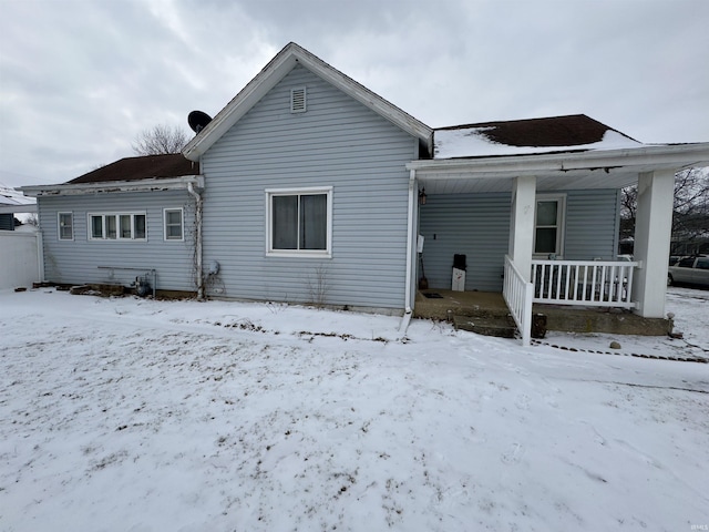 snow covered rear of property featuring covered porch