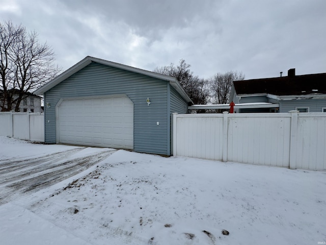 snow covered garage with a detached garage and fence