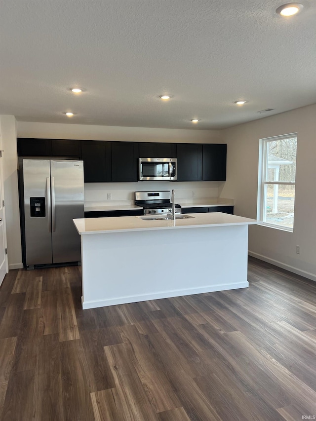 kitchen featuring dark cabinets, a kitchen island with sink, stainless steel appliances, and light countertops