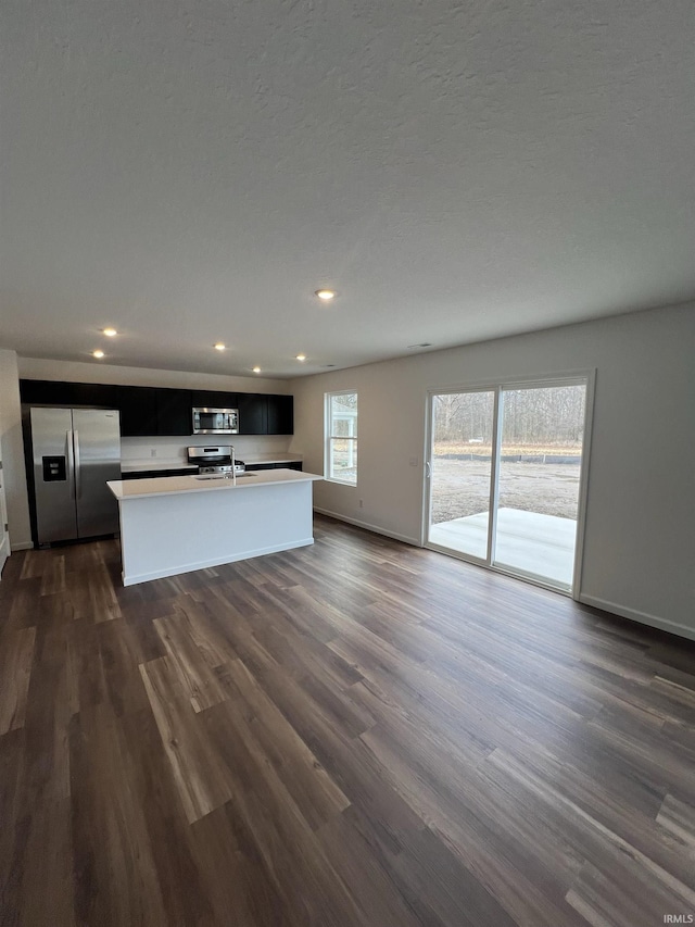 kitchen featuring appliances with stainless steel finishes, open floor plan, a kitchen island with sink, and dark wood-style floors