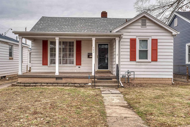 bungalow with covered porch, a shingled roof, a chimney, and a front yard