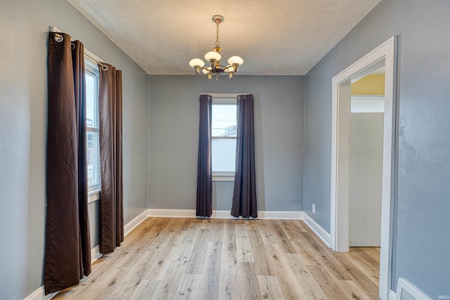 empty room featuring light wood finished floors, visible vents, baseboards, a textured ceiling, and a chandelier