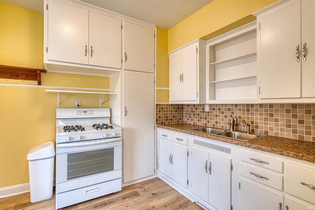 kitchen with light wood finished floors, white gas range, white cabinetry, open shelves, and a sink