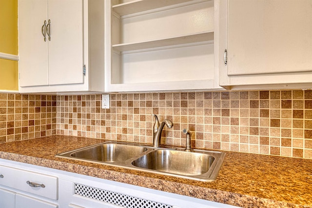 kitchen with tasteful backsplash, dark countertops, a sink, and white cabinets