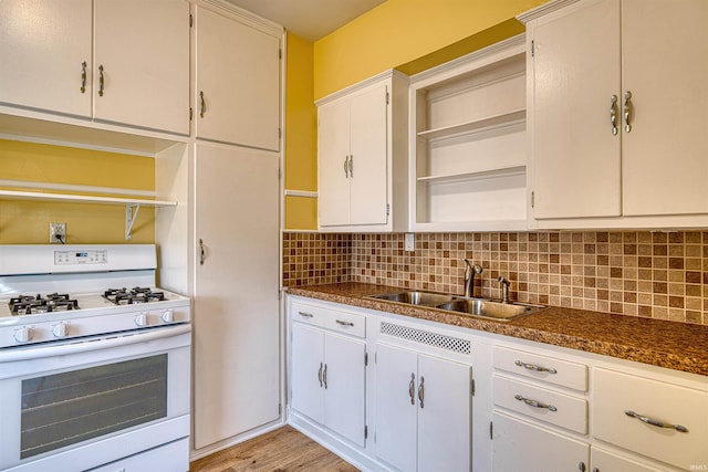 kitchen featuring open shelves, tasteful backsplash, white gas range, white cabinetry, and a sink