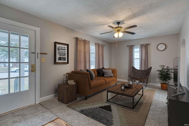 living room with a textured ceiling, ceiling fan, and baseboards