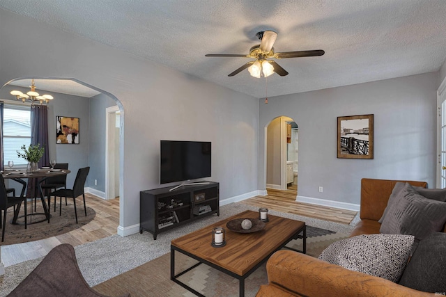 living area featuring baseboards, arched walkways, a textured ceiling, and ceiling fan with notable chandelier