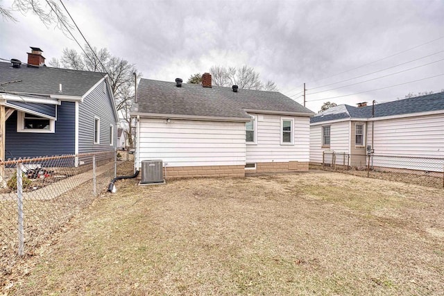 back of property with central AC, fence, a yard, roof with shingles, and a chimney