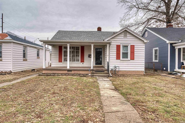 view of front facade featuring a shingled roof, a front yard, covered porch, and a chimney