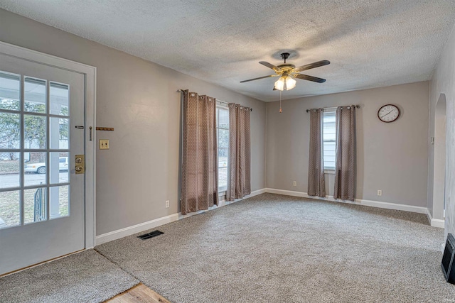 carpeted empty room with arched walkways, ceiling fan, a textured ceiling, visible vents, and baseboards