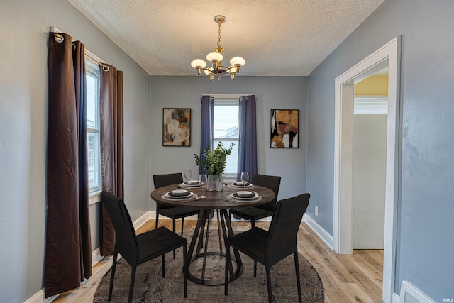 dining room with a textured ceiling, a notable chandelier, visible vents, baseboards, and light wood-style floors