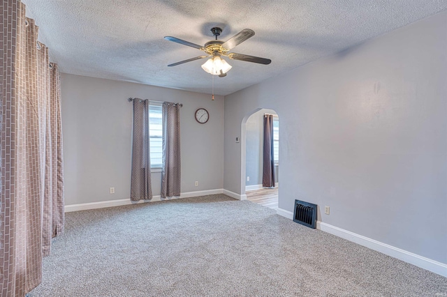 empty room featuring arched walkways, visible vents, baseboards, a ceiling fan, and carpet