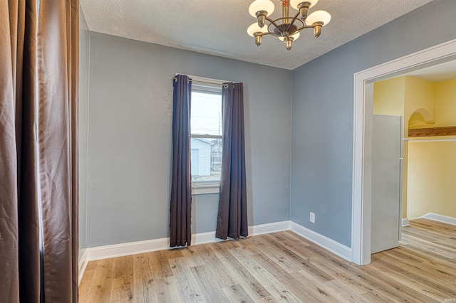 empty room featuring light wood-style floors, a notable chandelier, and baseboards