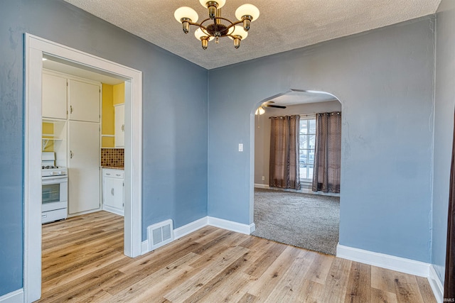 unfurnished dining area featuring arched walkways, a textured ceiling, visible vents, light wood finished floors, and an inviting chandelier