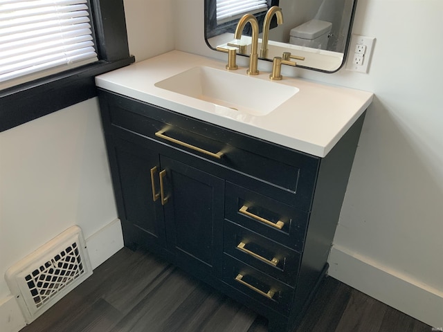 half bath featuring toilet, visible vents, wood finished floors, and vanity