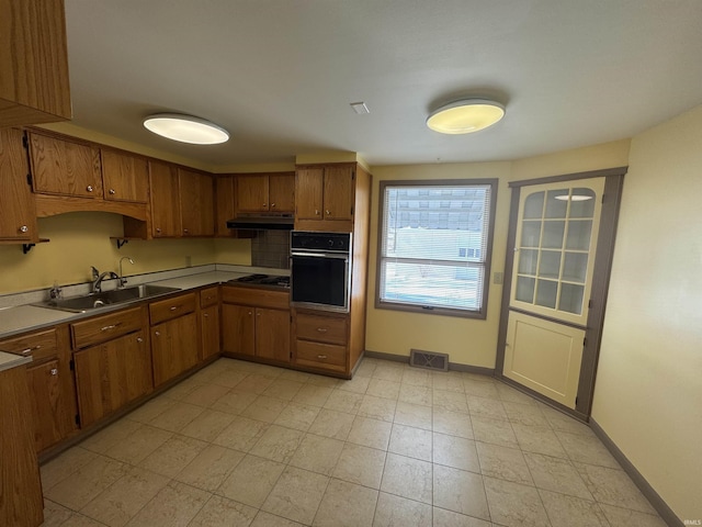 kitchen featuring visible vents, brown cabinetry, oven, under cabinet range hood, and a sink