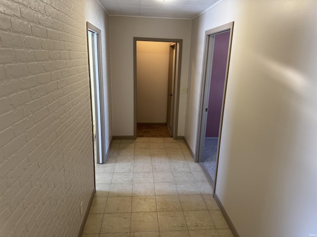 corridor with baseboards and brick wall