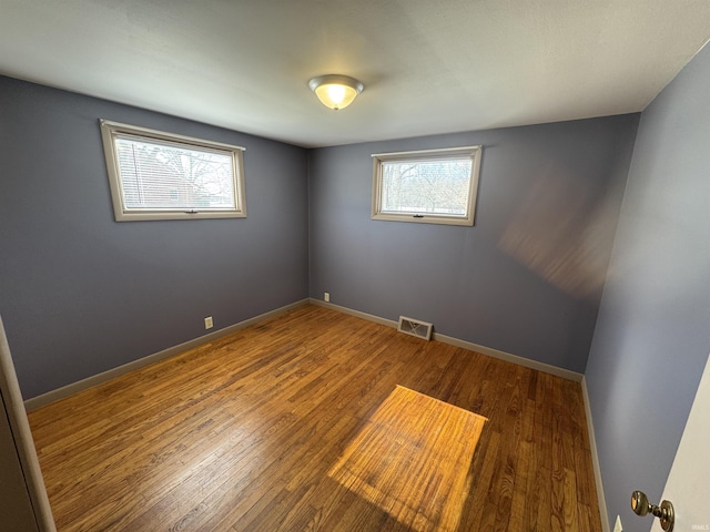 empty room with dark wood-type flooring, visible vents, and baseboards