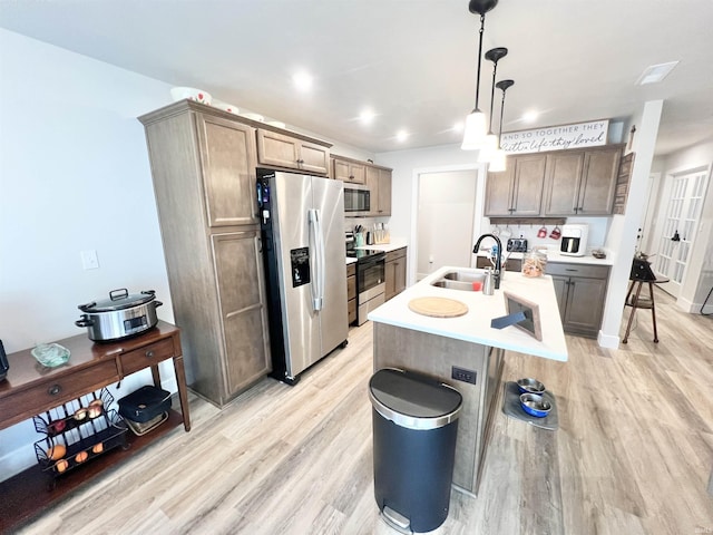 kitchen with decorative light fixtures, a center island with sink, light countertops, appliances with stainless steel finishes, and a sink