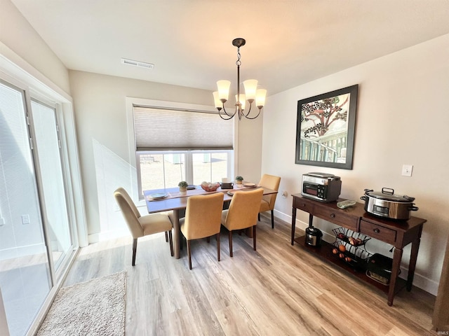 dining area featuring baseboards, light wood-style flooring, visible vents, and a notable chandelier