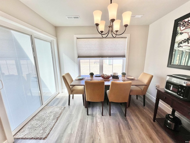 dining area with baseboards, visible vents, a chandelier, and wood finished floors