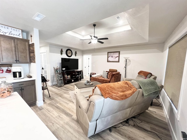 living room featuring baseboards, visible vents, a ceiling fan, light wood-style flooring, and a tray ceiling