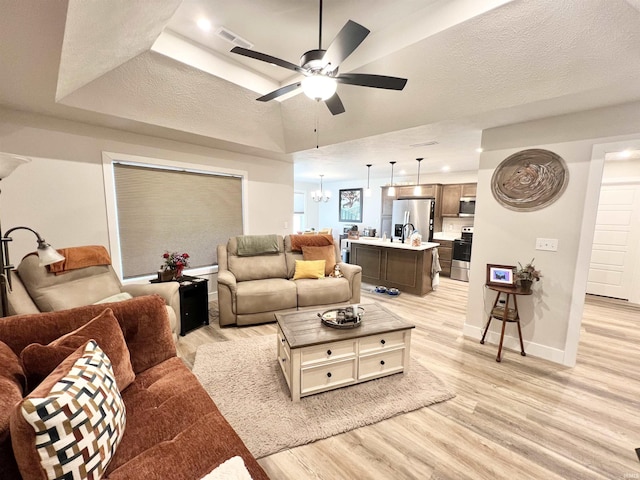 living room with light wood-style flooring, baseboards, a raised ceiling, and a textured ceiling