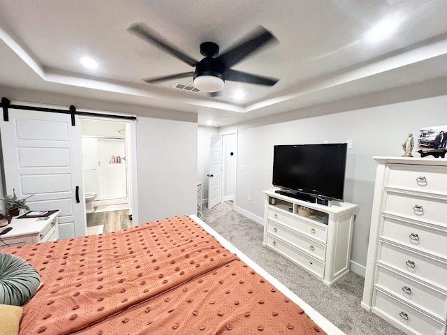 bedroom with a raised ceiling, a barn door, light carpet, connected bathroom, and baseboards