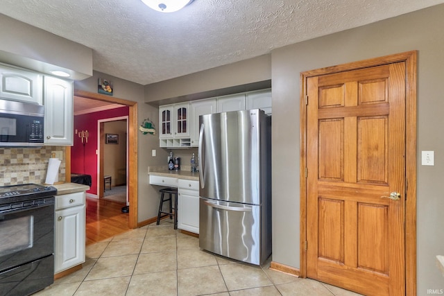 kitchen with appliances with stainless steel finishes, white cabinets, light countertops, and glass insert cabinets