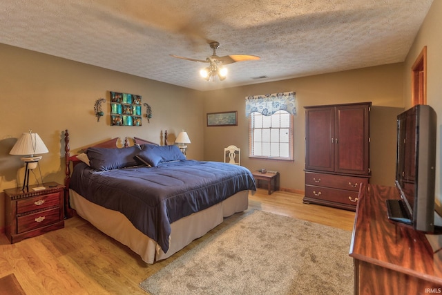 bedroom featuring light wood-style floors, visible vents, a textured ceiling, and a ceiling fan