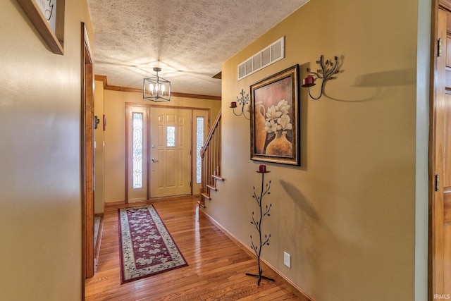 foyer featuring a textured ceiling, wood finished floors, visible vents, baseboards, and crown molding