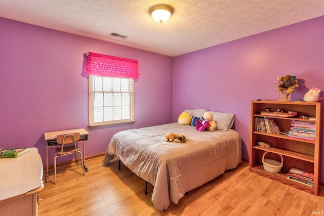 bedroom featuring light wood-style floors, baseboards, visible vents, and a textured ceiling