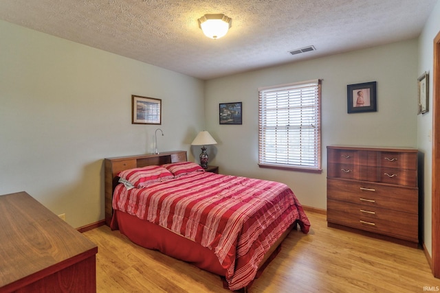 bedroom with light wood-style floors, visible vents, a textured ceiling, and baseboards