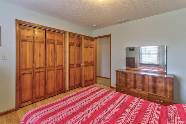 unfurnished bedroom with a textured ceiling, light wood-type flooring, baseboards, and multiple closets