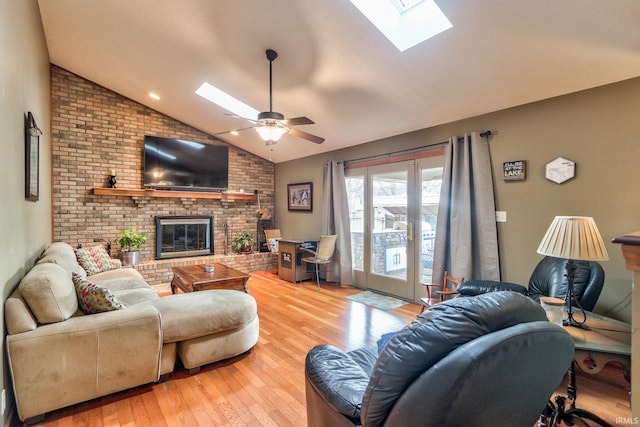 living area featuring light wood finished floors, vaulted ceiling with skylight, a ceiling fan, brick wall, and a fireplace