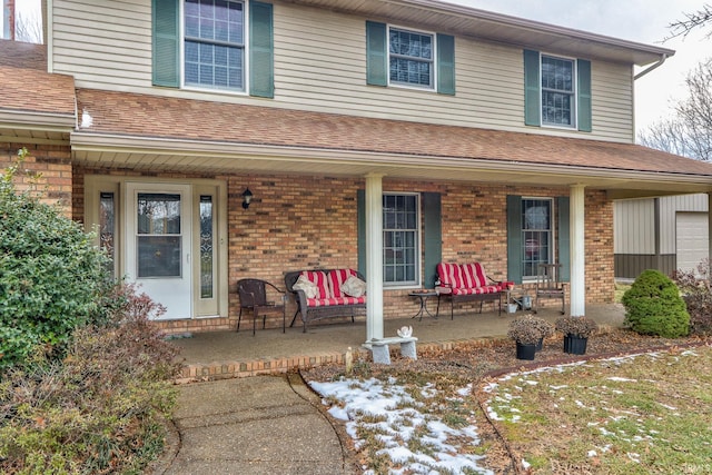 view of front of home featuring a shingled roof, covered porch, and brick siding